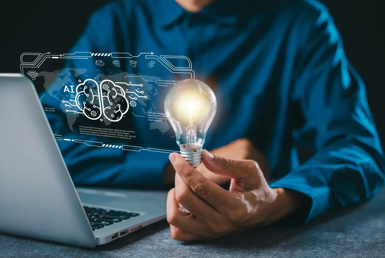 Professional in a blue shirt holding an illuminated light bulb beside a holographic AI brain and world map projected from a laptop