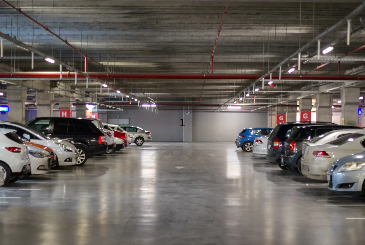 Wide view of a busy underground parking garage with vehicles parked along both sides and lettered zone signage